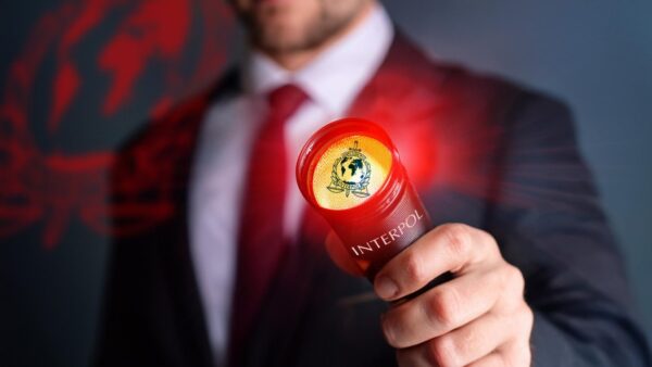 A man in a suit holds an INTERPOL branded red torch, which lights up the shape of the INTERPOL logo in red, to depict an INTERPOL red notice.