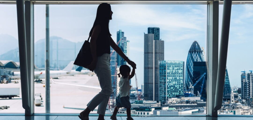 To refer to the 'remittance basis' section of this tax guide for Hong Kong residents, an image of a mother and child walking past a glass window at an airport can be seen. On the left-hand side, the background is that of an airport, with aeroplanes. On the right hand side, the background shows the London cityscape. 