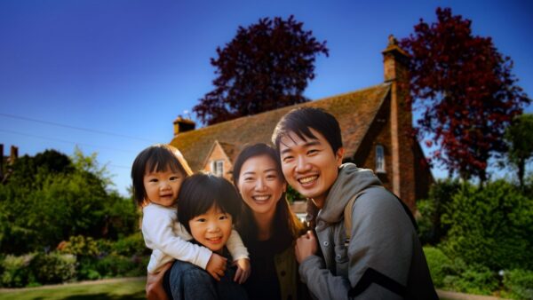 A Hong Kong family are in the foreground, in front of a residential UK property, exploring how this article helps explain the UK property purchase system to Hong Kong buyers.