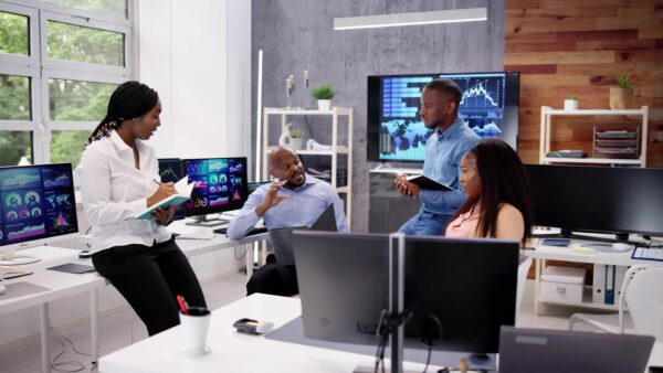 Four tech professionals sit in a meeting, with screens around them, showing the opportunities available to tech professionals moving to the UK.