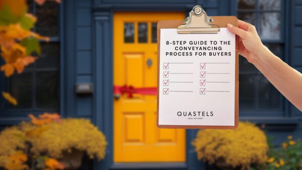 A person holds a clipboard in front of a vibrant yellow front door decorated with a red ribbon. The clipboard displays a checklist titled "8-Step Guide to the Conveyancing Process for Buyers" with all eight items checked off. Autumn leaves and potted yellow flowers are visible around the doorway, suggesting a cozy, welcoming home. The bottom of the checklist reads "QUASTELS Legal Advisers.