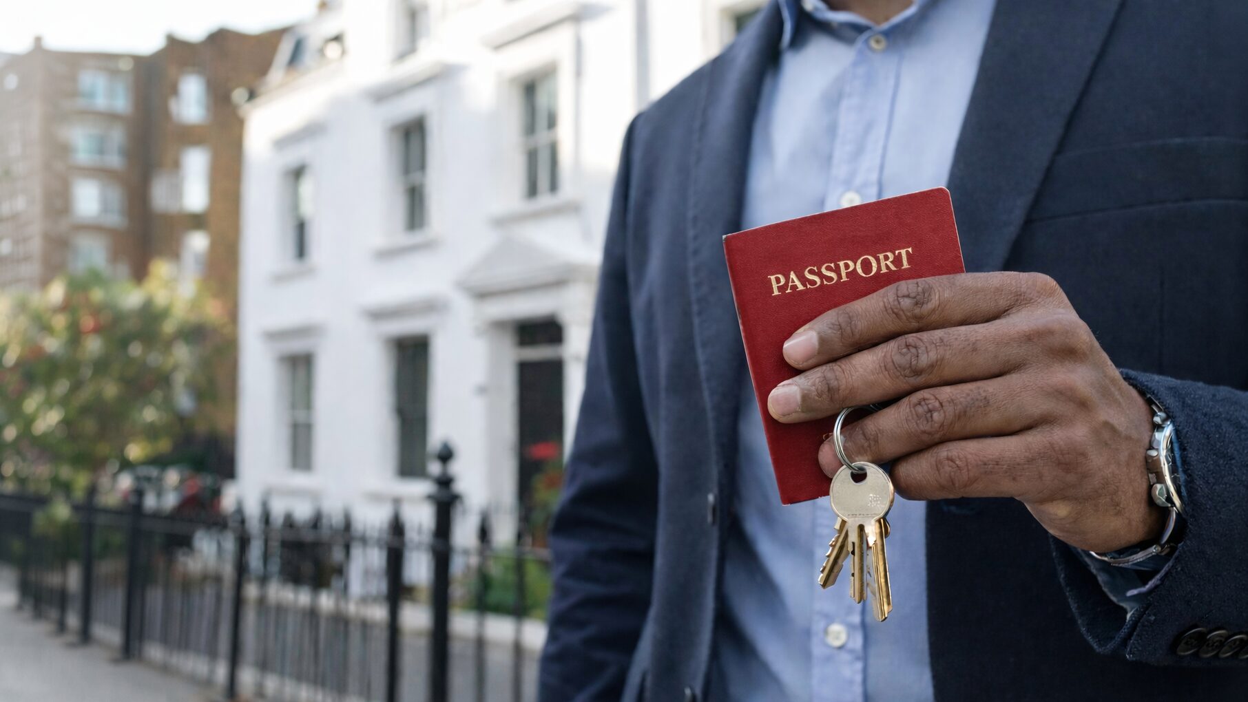 A man stands outside of his new London property holding the keys and his passport to represent that he is an overseas buyer purchasing property in the UK.