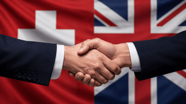 Hands shaking in front of Swiss flag and Union Jack, to represent the UK-Switzerland trade agreement.
